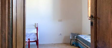 A room with wooden floors, a bed with a patterned bedspread, a chair, and a wooden door.