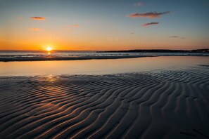 Una playa al atardecer con ondulaciones en la arena y un mar tranquilo.