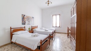 Een hotelkamer met drie houten bedden, een groot raam en een houten garderobe.