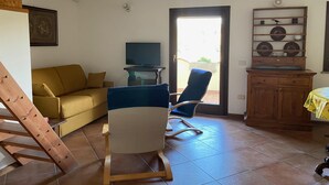 A living room with a sofa, a blue chair, a television, and a wooden cabinet. - Il Carrubo in Torre Grande (Oristano)