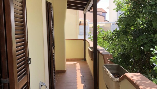 A corridor with a tiled floor, wooden doors, and a planter box. - Il Carrubo in Torre Grande (Oristano)