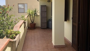 A corridor with a tiled floor, potted plants, a refrigerator, and a door. - Il Carrubo in Torre Grande (Oristano)