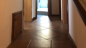 A hallway with wooden ceiling and tiled floor, leading to a bright room with a window. - Il Carrubo in Torre Grande (Oristano)