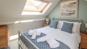 A bedroom with a skylight, a bed with white and patterned bedding, a nightstand with a lamp, and a framed picture on the wall. - Little Gull Cottage (Weymouth)