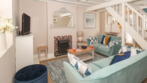 A living room with a fireplace, a sofa, a television, and a staircase. - Little Gull Cottage (Weymouth)