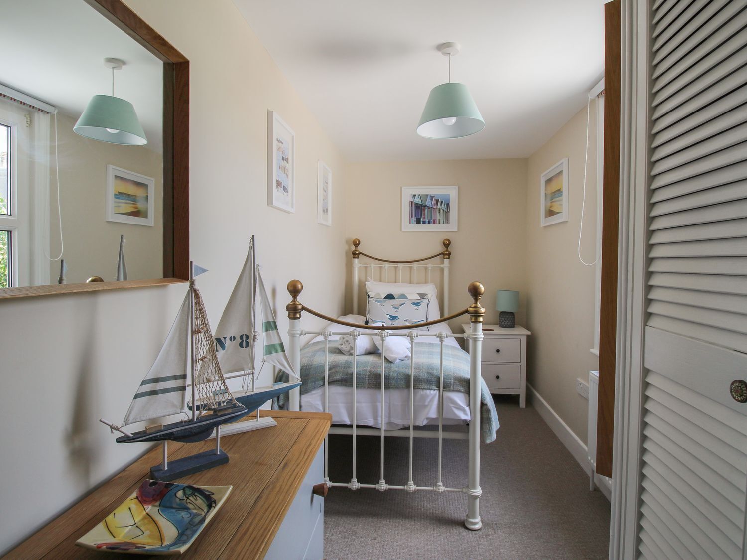A bedroom with a bed, a nightstand, a dresser, a sailboat model, and a mirror.