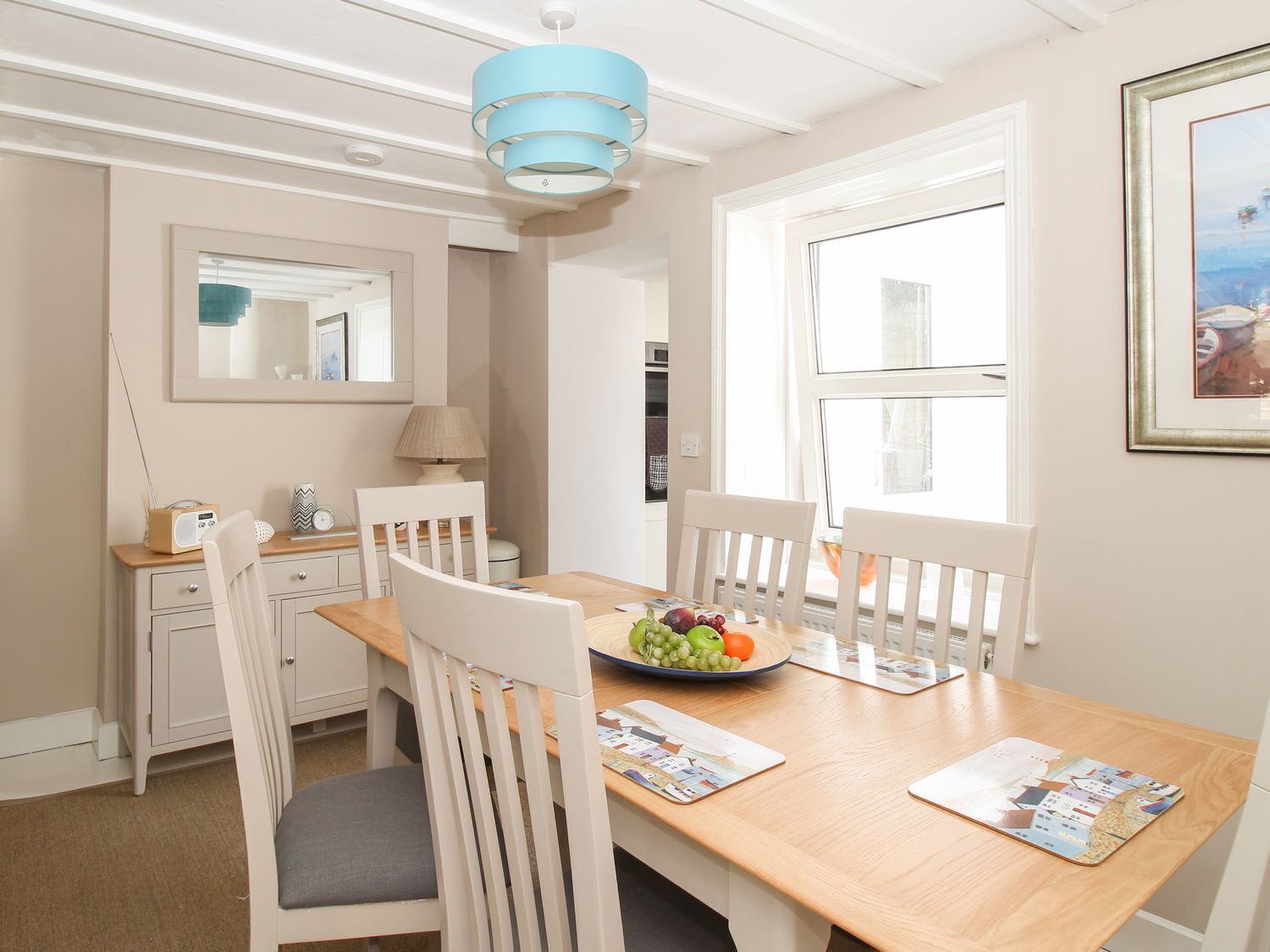 A dining area with a wooden table, white chairs, a blue pendant light, a mirror, and a framed picture on the wall.