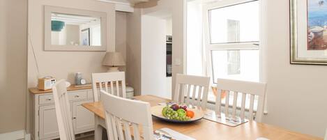 A dining area with a wooden table, white chairs, a blue pendant light, a mirror, and a framed picture on the wall.
