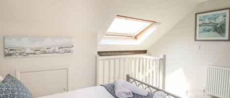A bedroom with a skylight, a bed with white linens, a white radiator, and a painting on the wall.