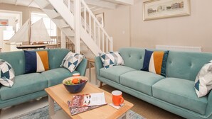 A living room with two teal sofas, a wooden coffee table, and a sailboat model. - Little Gull Cottage (Weymouth)