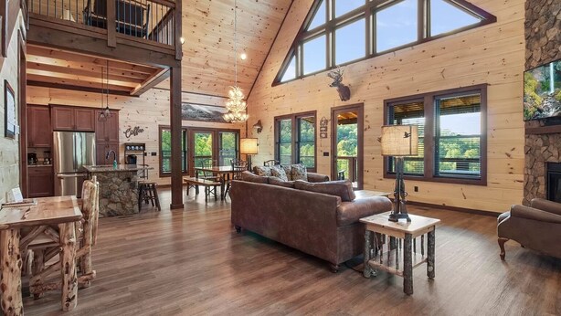 A spacious living area with a high ceiling, wooden floors, a fireplace, and large windows offering views of the outdoors. - Gorgeous 4BD w/ VIEWS! Theater +Firepit +Game Room (Sevierville)