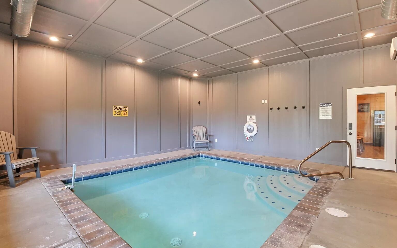 A swimming pool with a caution sign, a lifebuoy, and a chair.