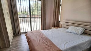 A bedroom with a bed, wooden floor, and a view through a window with curtains. - Modern 1 -bed Room Apartment in Grand Baie (Grand-Baie)