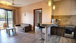 A modern kitchen with a built-in oven, a dining area with a bar stool, and a sofa. - Modern 1 -bed Room Apartment in Grand Baie (Grand-Baie)