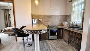 A compact kitchen with a round dining table, two bar stools, a built-in oven, and a sink. - Modern 1 -bed Room Apartment in Grand Baie (Grand-Baie)