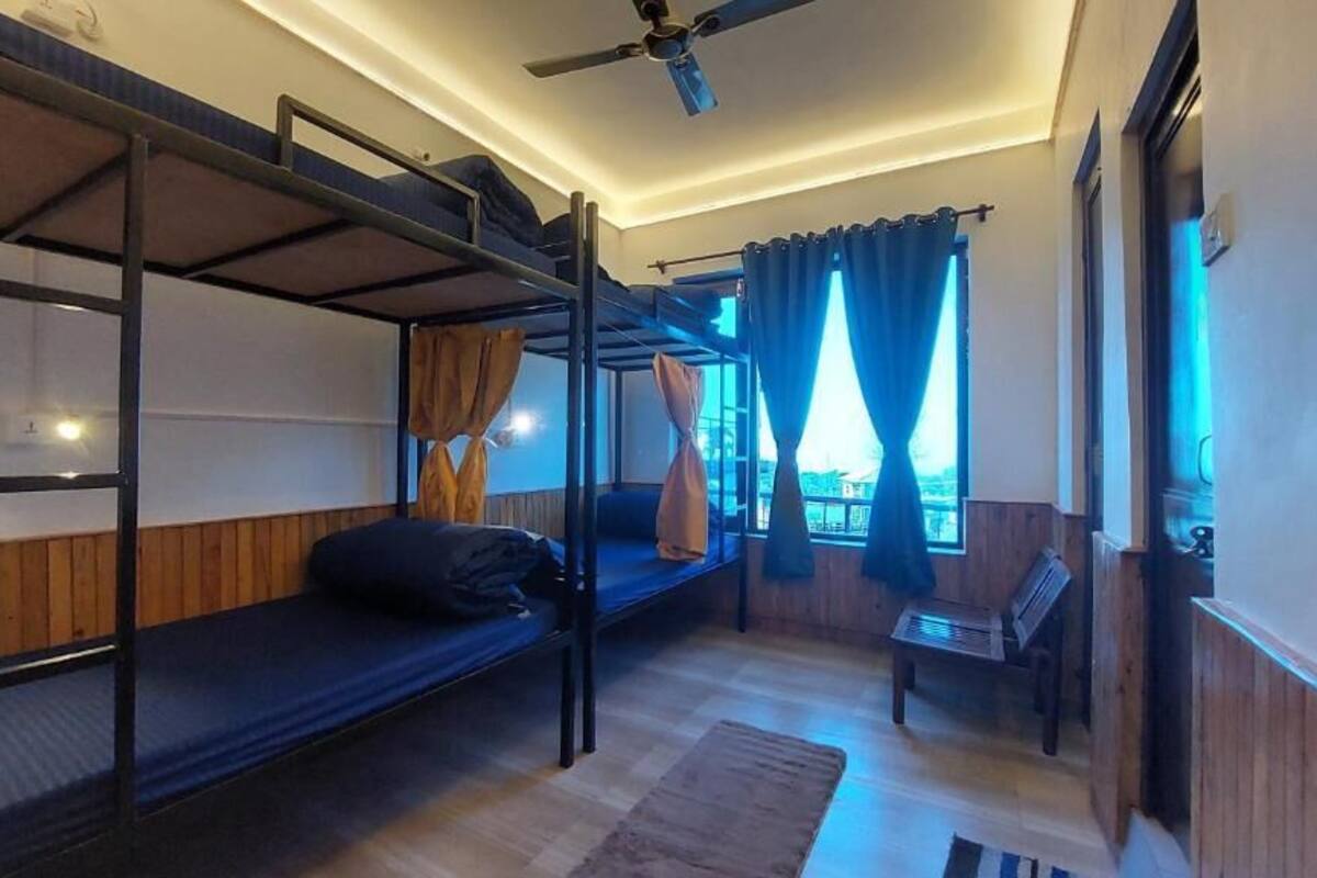 Een studentenkamer met stapelbedden, een plafondventilator, een raam met gordijnen en een klein tafeltje.