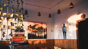 A cozy room with a wooden wall, a large tapestry, and a stack of board games. - The Hostel Stories Bir - Landing Site (Baijnath)