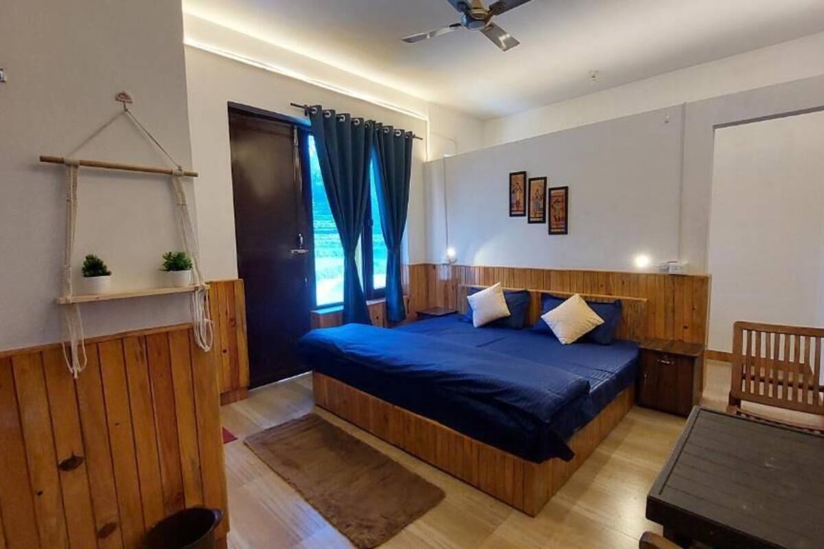 Een slaapkamer met een bed, een houten hoofdbord, nachtkastjes, een kleine houten stoel, een hangplant en een raam met gordijnen.