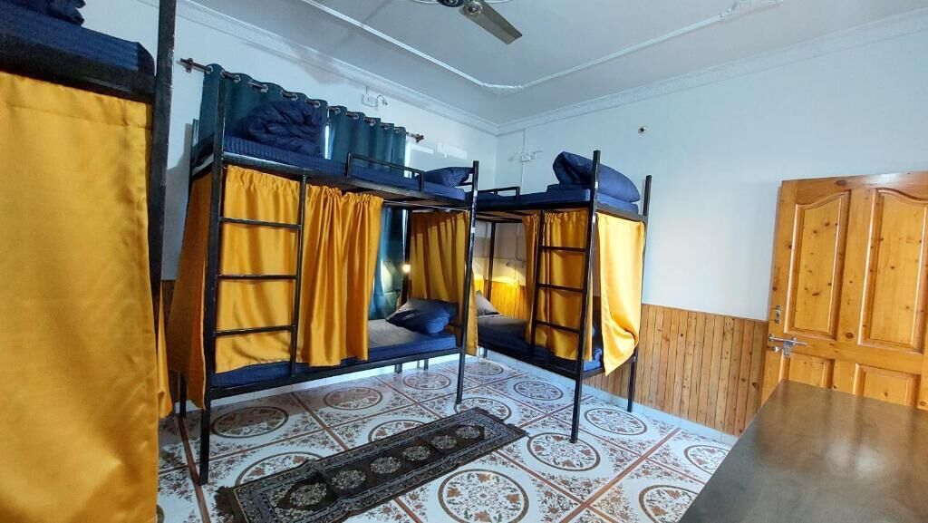 Ett sovsalsrum med våningssängar, en takfläkt och en mönstrad matta.