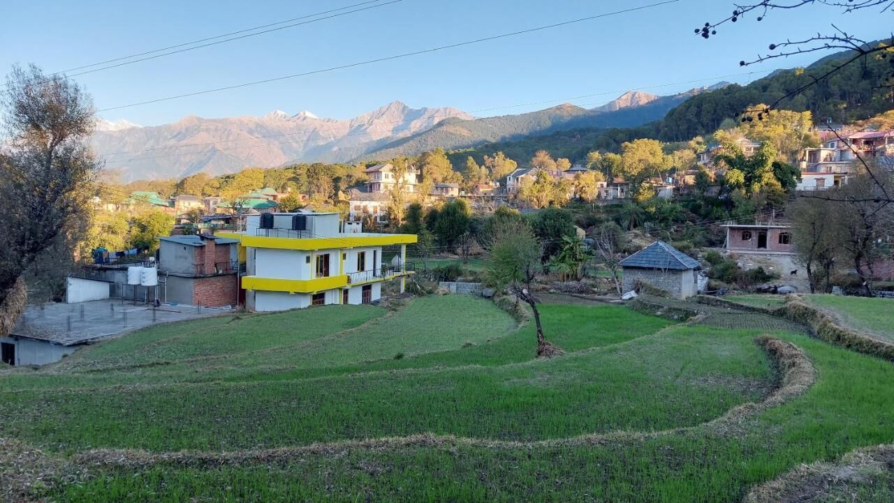 Un pueblo rural con campos en terrazas, un edificio amarillo y blanco, y montañas al fondo.