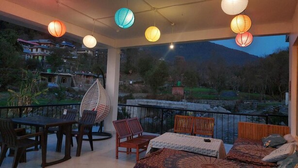 A balcony with a table and chairs, a hanging chair, and a bed with a patterned bedspread. - The Hostel Stories Bir - Landing Site (Baijnath)