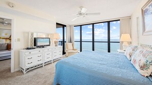 Un cuarto de hotel con una cama grande, televisión, tocador y vista al océano.