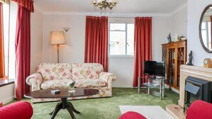 A living room with a floral sofa, a coffee table, a TV, and a fireplace. - Bay View Esplanade Apartment Overlooking Harbour (Oban)