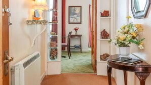 A hallway with a radiator, a lamp, a mirror, and a table with a vase of flowers. - Bay View Esplanade Apartment Overlooking Harbour (Oban)