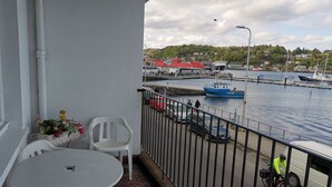 A balcony with a table and chairs, overlooking a marina with boats and a red-roofed building in the background. - Bay View Esplanade Apartment Overlooking Harbour (Oban)