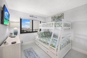 A child's bunk bed with a view of the sea through a window, a desk with a lamp, and a small plant. - Breath-Taking Beachfront Condo | Pool/Spa/Views (Marco Island)