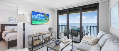 Ein stilvolles Wohnzimmer mit einer Couch, einem Couchtisch und einem Fernseher, der eine Strandansicht zeigt.