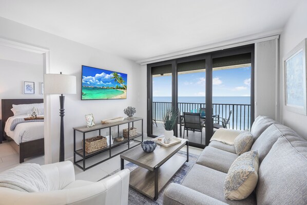 A modern living room with a sofa, coffee table, and a TV displaying a beach scene.