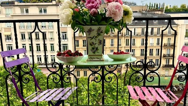 Un balcón con una mesa, dos sillas, un florero con flores y un cuenco de fresas.