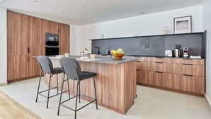 A modern kitchen with wooden cabinetry, a central island with bar stools, and a built-in oven. - Luxurious apartment Louvre Museum-Palais Royal (Paris)
