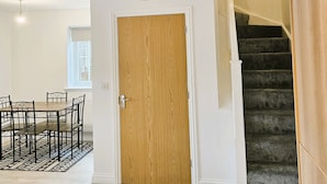 Una stanza con una porta in legno, un tavolo da pranzo con sedie e un pavimento con tappeto.