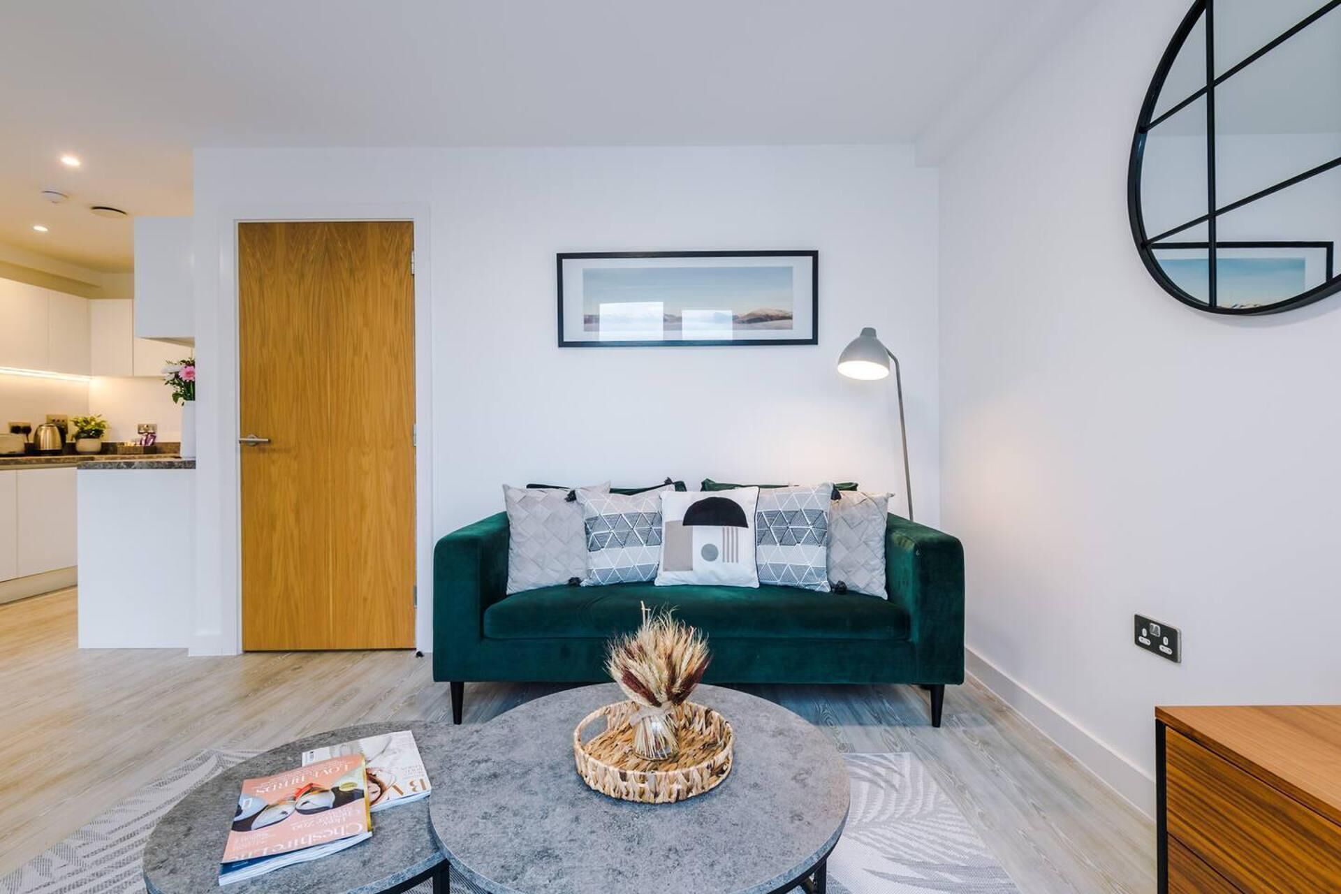 A modern living room with a green sofa, a round coffee table, and a framed picture on the wall.