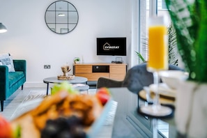 A modern living room with a teal sofa, a round coffee table, and a TV displaying 'EVERSTAY RENTALS'. - Manchester Short Stay (Salford)