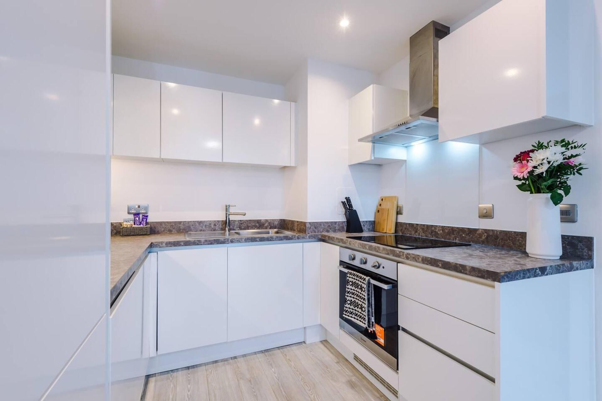 A modern kitchen with white cabinets, a granite countertop, a built-in oven, and a stainless steel range hood.