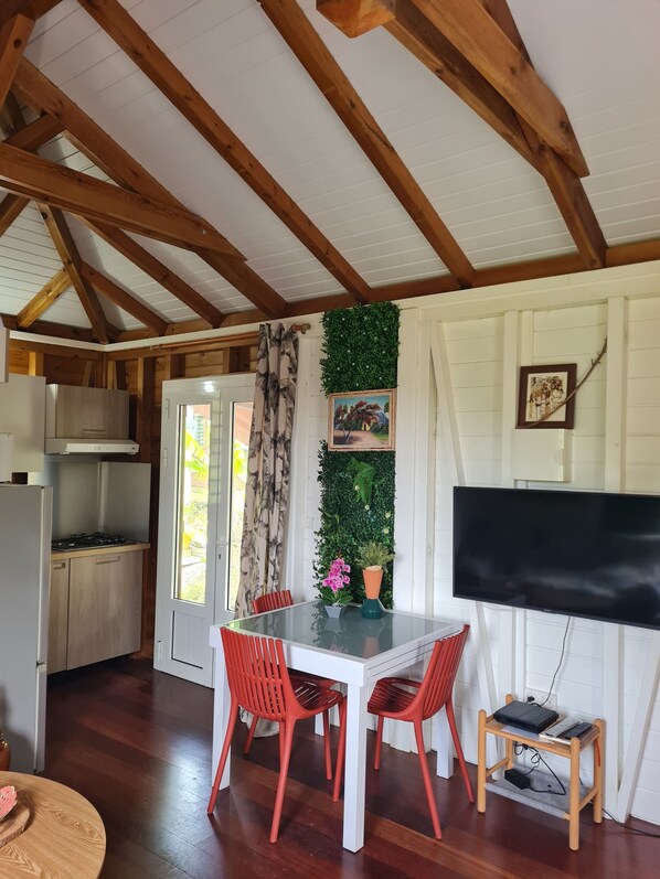 Une cuisine avec des poutres en bois, une table à manger avec des chaises rouges, un téléviseur et une petite table d’appoint en bois.