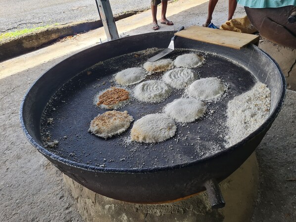 Un grand espace extérieur aménagé pour la cuisine, avec un barbecue noir, plusieurs aliments de forme ronde en train de cuire, et une personne se tenant à proximité.