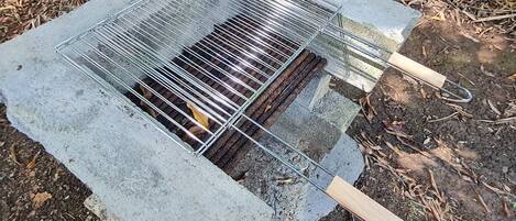 A portable grill with a metal grate and wooden handles, placed on a concrete base outdoors.