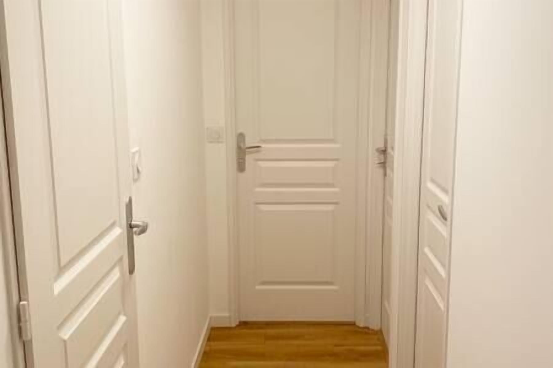 A narrow hallway with white doors on both sides and a wooden floor.