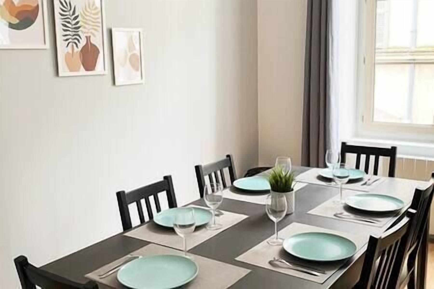 A dining table set with teal plates, wine glasses, and a small potted plant.