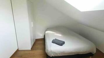 Een kleine eenpersoonskamer met een schuine plafond en een houten vloer.