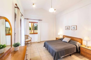 A bedroom with a bed, bedside table, lamp, chair, and a window with curtains. - Villa Evanthia Polis (Poli Crysochous)