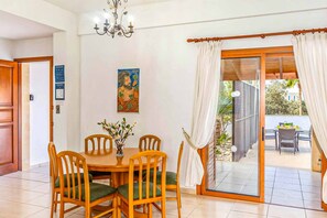 A dining area with a wooden table and chairs, a chandelier, and a painting on the wall. - Villa Evanthia Polis (Poli Crysochous)