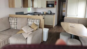 A compact RV interior with a kitchenette, a sofa with cushions, and a small dining table. - 208 Unity Beach 6 Berth enc Garden no Pets (Burnham-on-Sea)