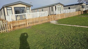 A row of mobile homes with white railings and a wooden fence. - 208 Unity Beach 6 Berth enc Garden no Pets (Burnham-on-Sea)