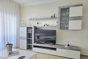 A modern living room with a flat-screen TV, built-in shelves, and a dining area with a table and chairs.