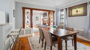 Un comedor con una mesa y sillas de madera, un ventilador de techo blanco y un ventanal con vidrieras.